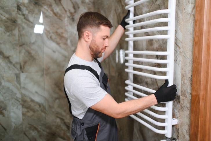 Ein Installateur baut einen Heizkörper im Badezimmer ein